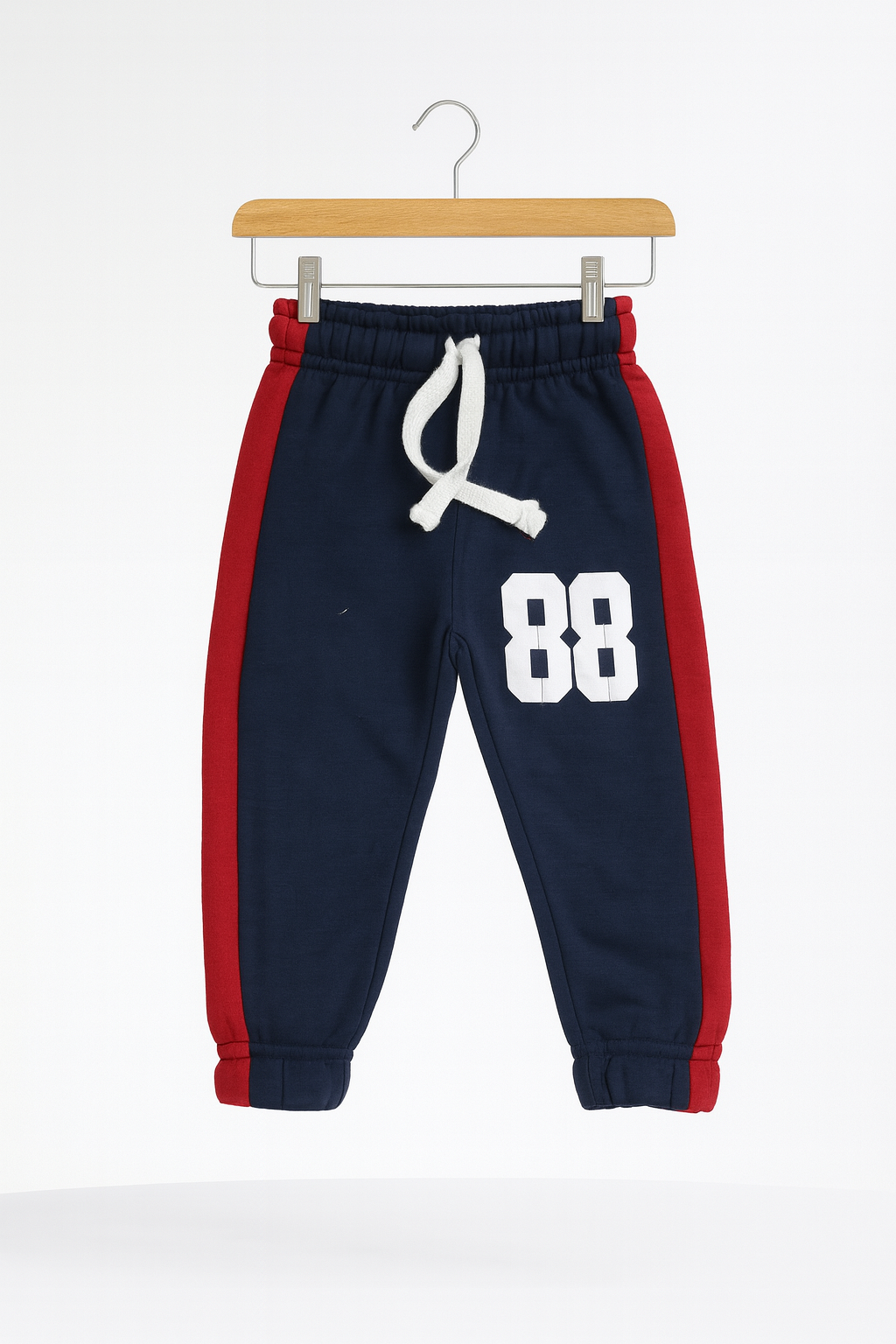 Confident 88 Kids Tracksuit trousers in navy with red side panels and white 88 print hung on a wooden hanger.